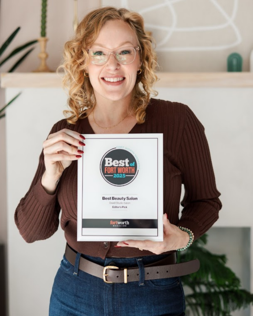 Smiling stylist holding a Best Beauty Salon award plaque from Fort Worth Magazine.