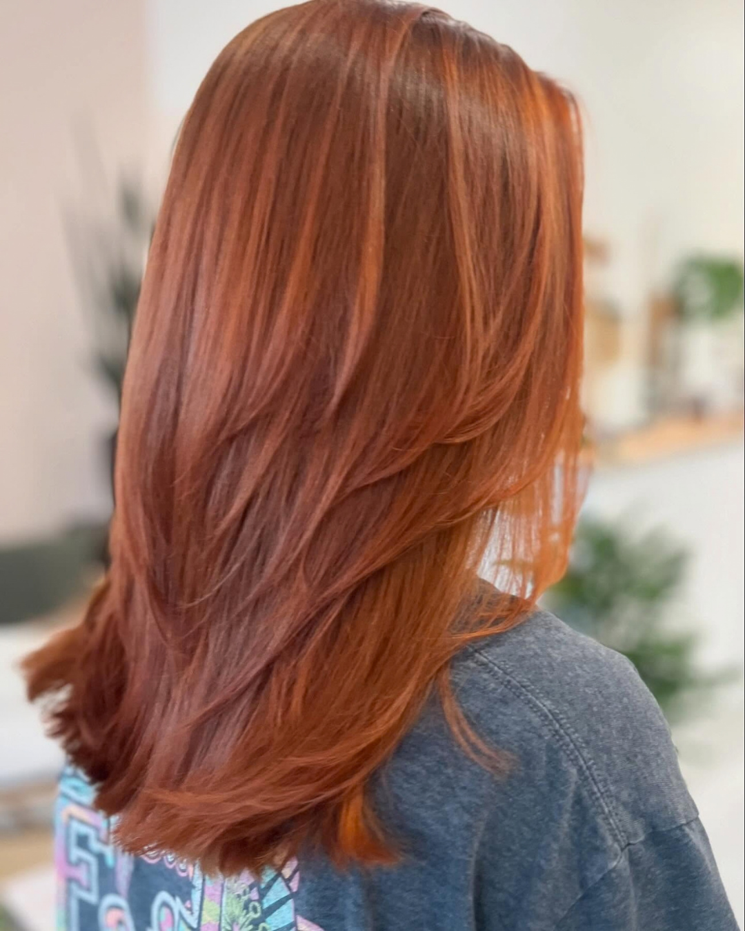 Back view of medium-length vibrant copper hair styled with face-framing layers by Ashley.