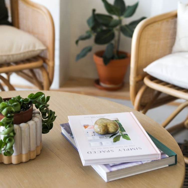 Coffee table with books and decor centered between rattan chairs at a friendly hair salon in West Fort Worth, Texas.