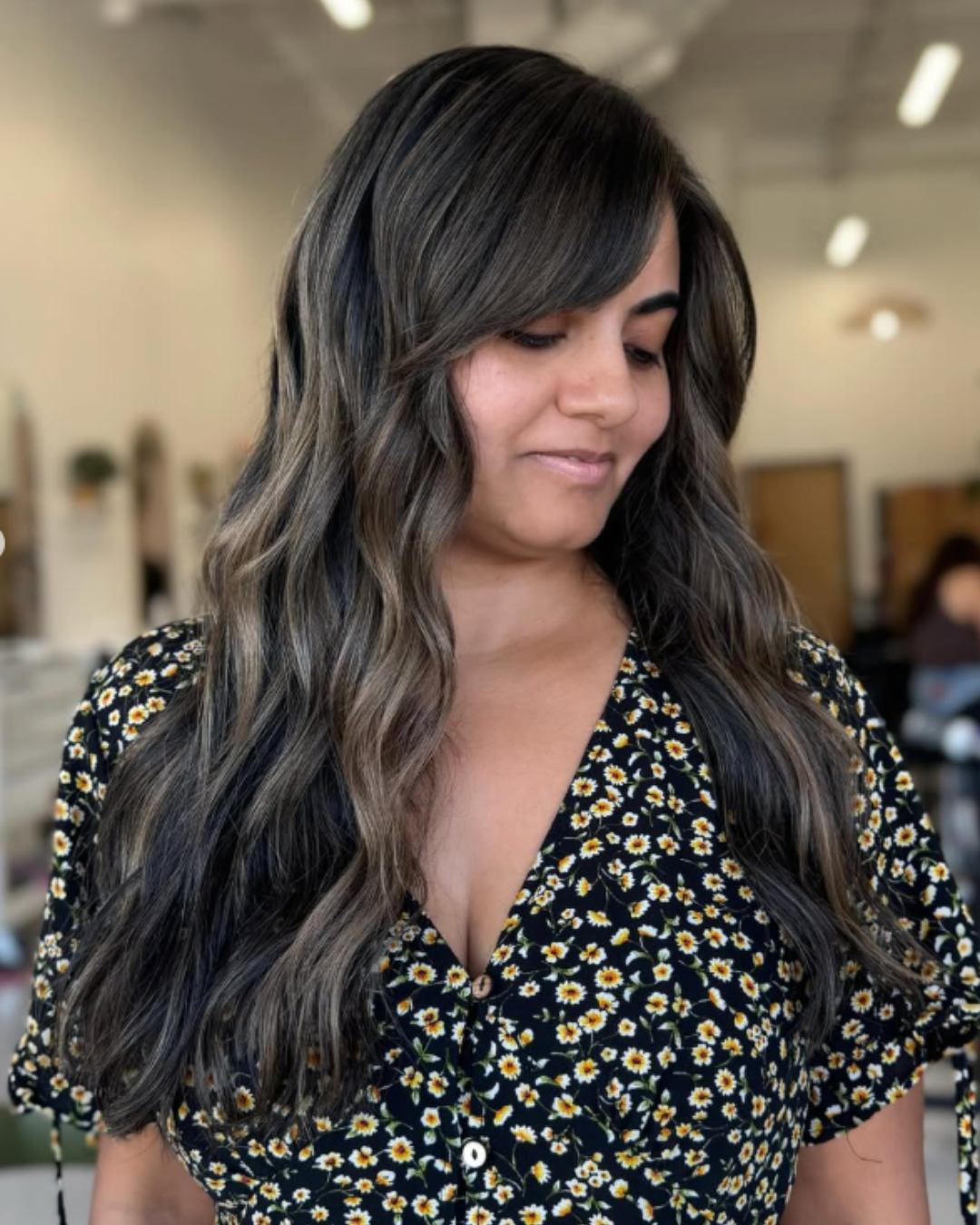 Front view of a woman with long, dark brown hair featuring soft highlights and face-framing layers by Zoe.