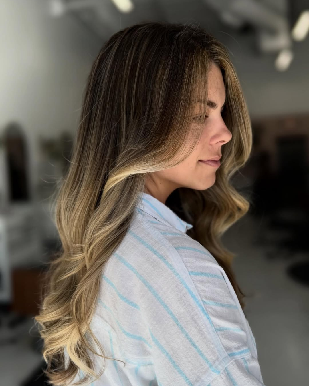 Long layered brunette hair with face-framing blonde highlights and soft waves by Jessica.