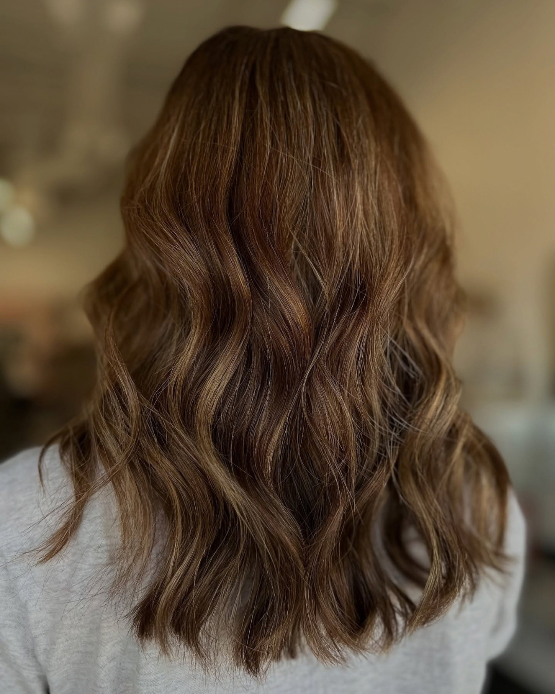 Medium-length brown hair with modern gray-blended coverage and loose waves by Ashley.