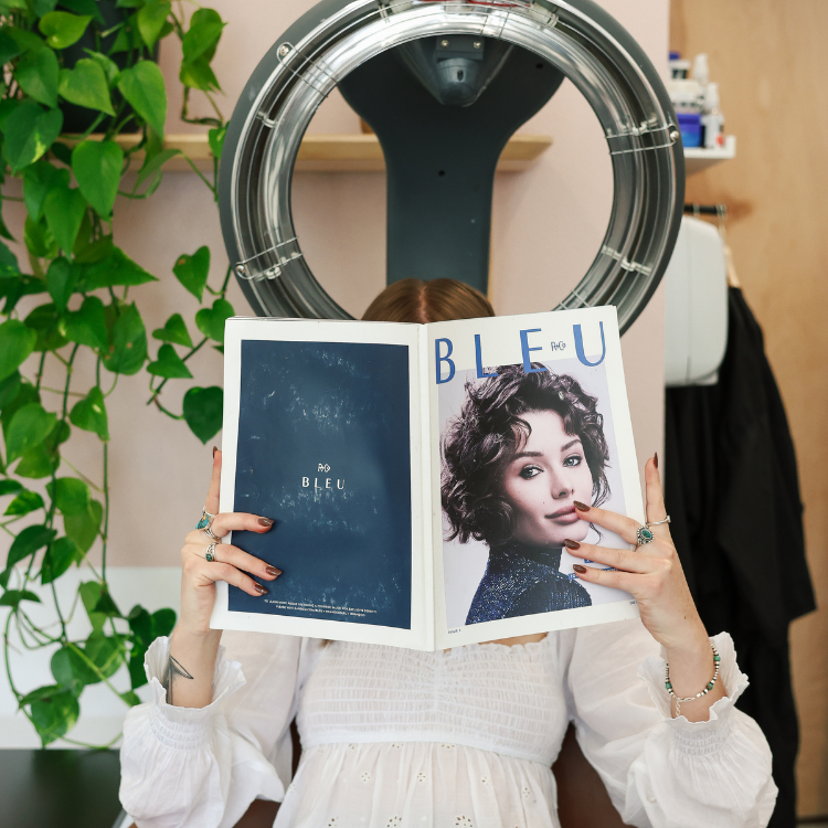 Client reading a magazine under a hooded salon hair dryer during a relaxing salon experience in Dallas-Fort Worth, Texas.