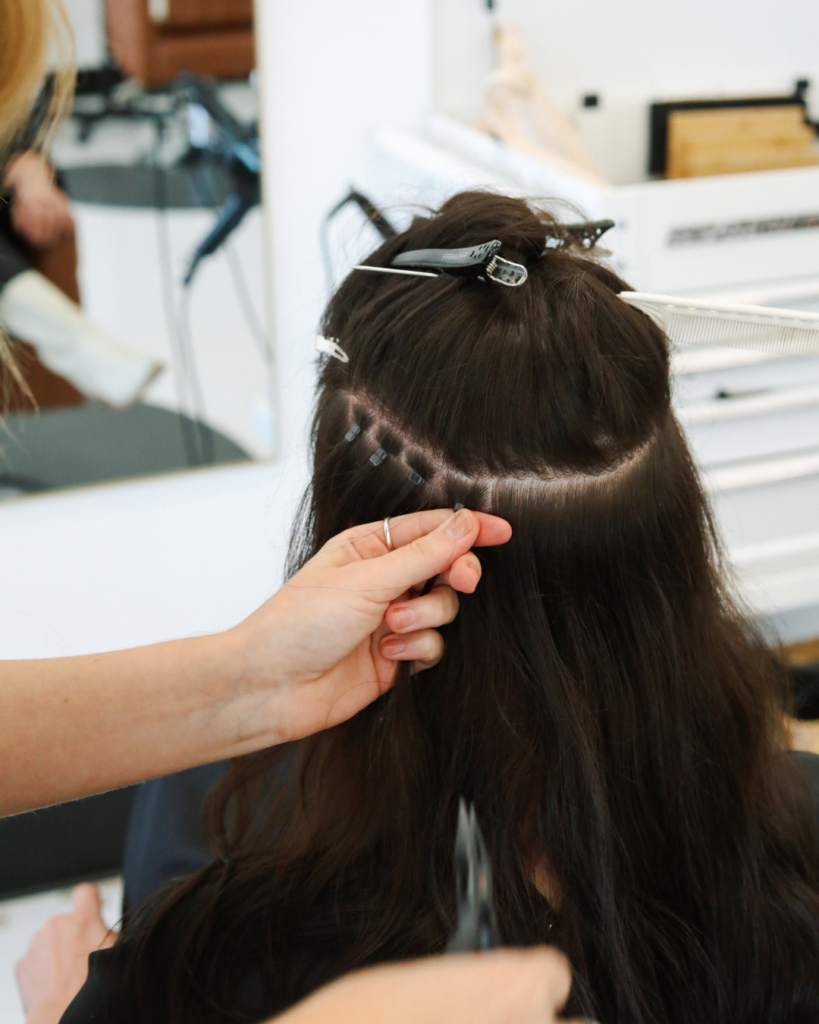 Close-up of hair sectioning and micro-beads during a sew-in hair extension installation at Dwell Studio Salon.