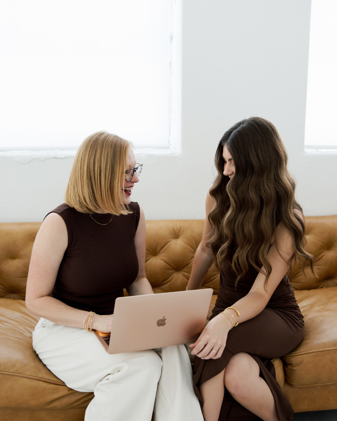 Two stylists laughing and reviewing work on a laptop during a supportive salon career consultation in Fort Worth.